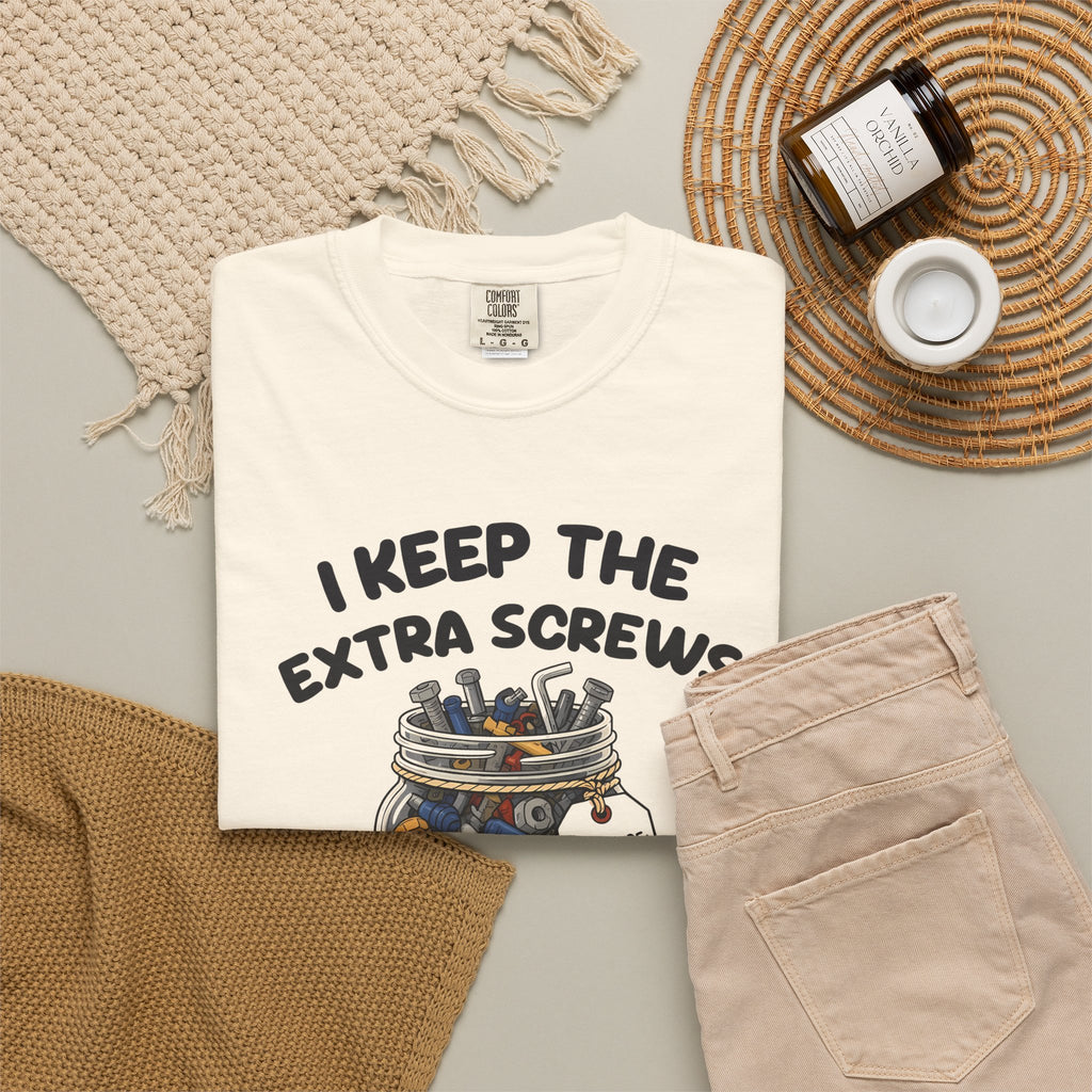 Ivory I Keep the Extra Screws tee by Mildly Unavailable laid flat with folded pants and home decor