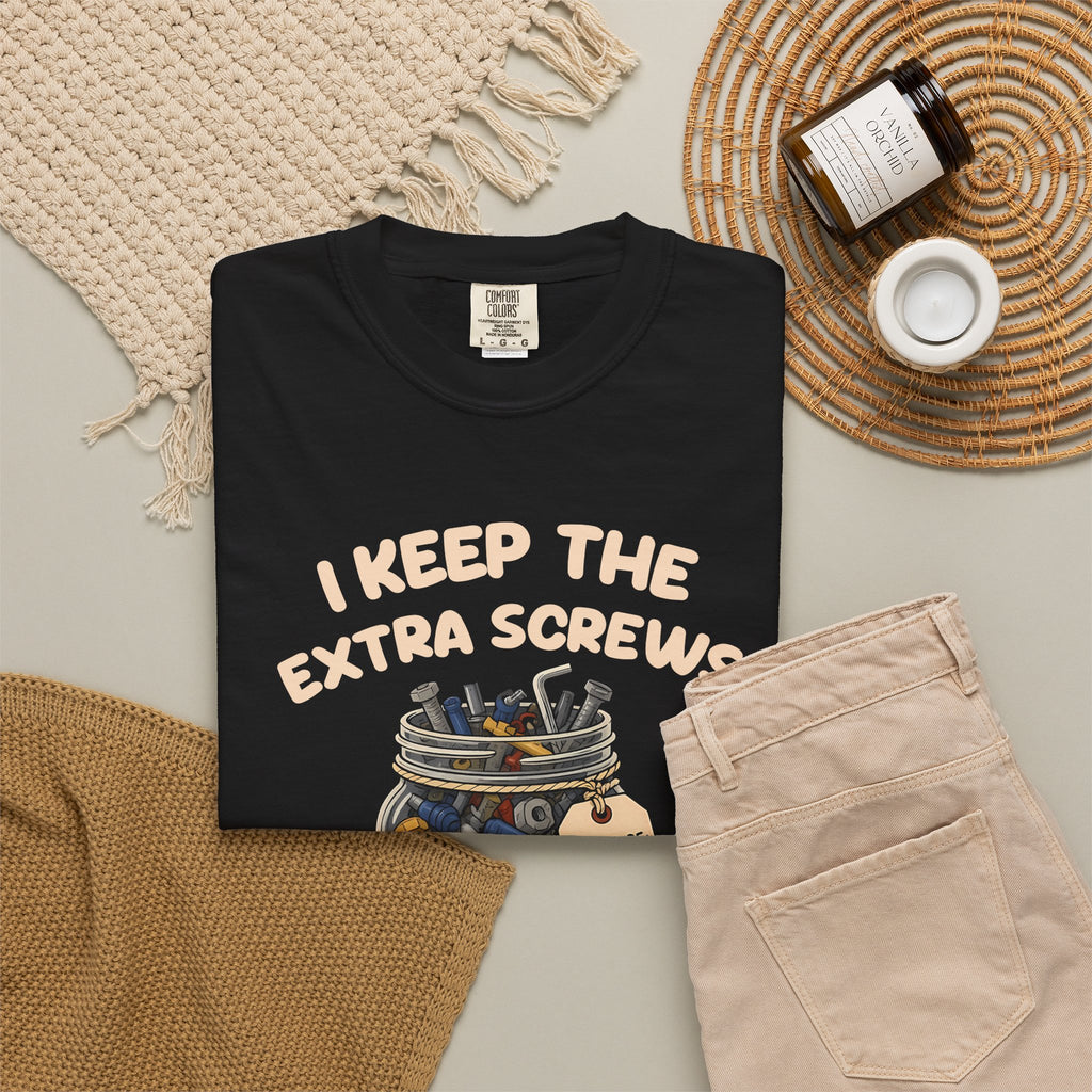 Black I Keep the Extra Screws tee by Mildly Unavailable laid flat with folded pants and home decor