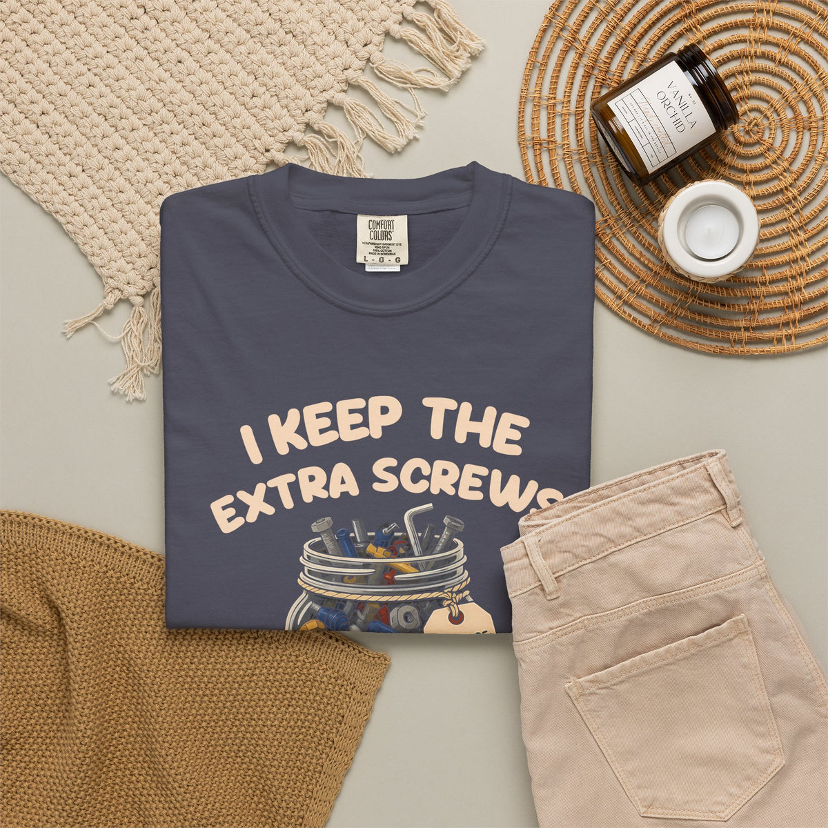 Navy I Keep the Extra Screws tee by Mildly Unavailable laid flat with folded pants and home decor