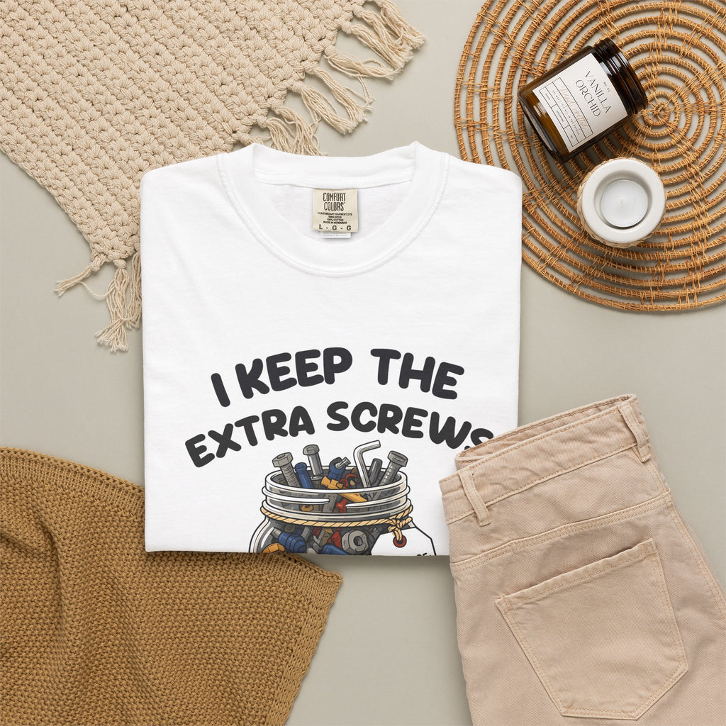 White I Keep the Extra Screws tee by Mildly Unavailable laid flat with folded pants and home decor